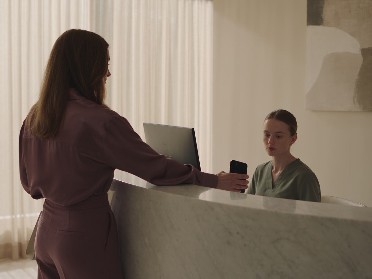 A visitor shares the details on their phone with a receptionist at the clinic counter