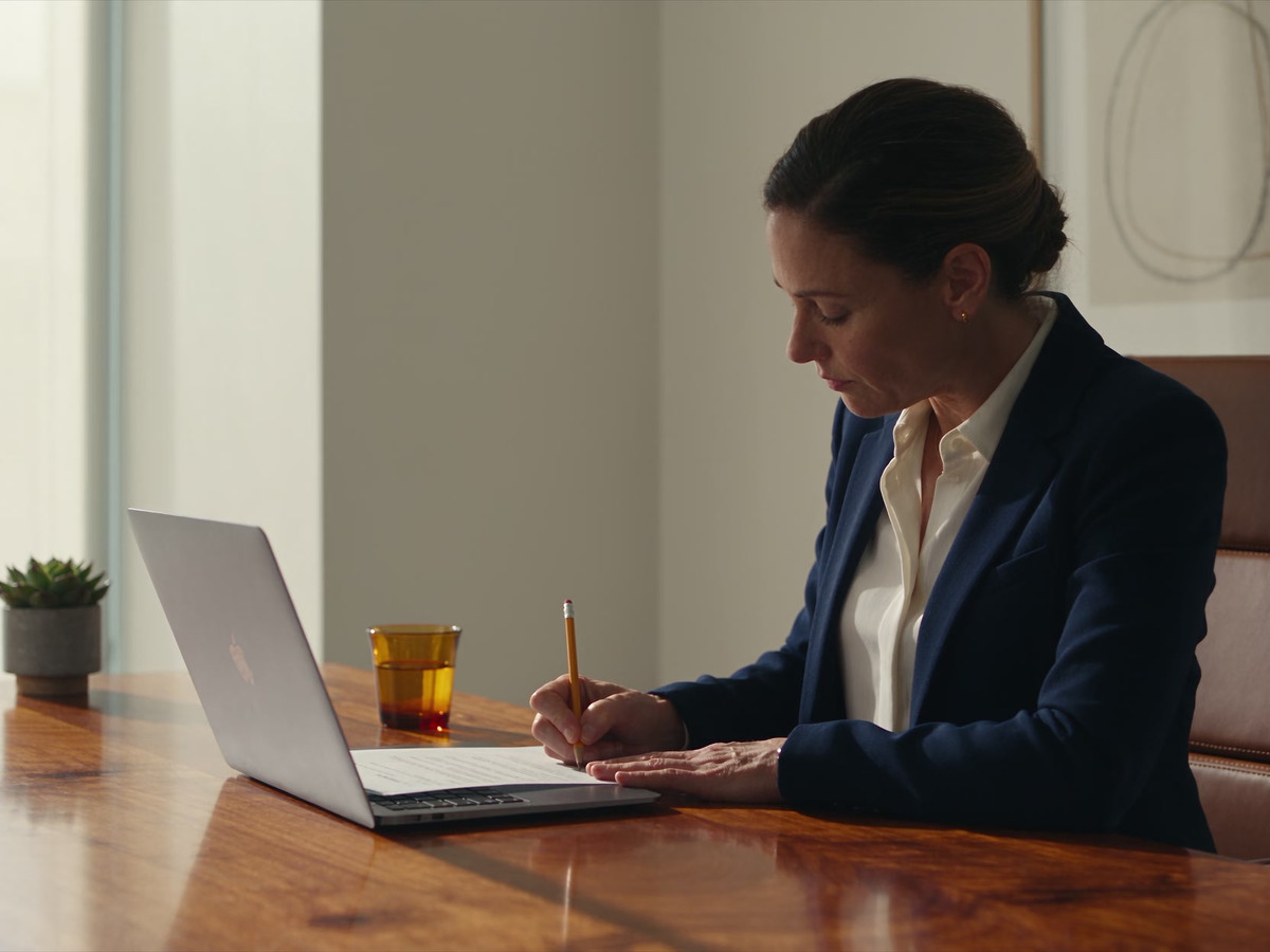 A clinic manager compares records and makes a note beside a laptop