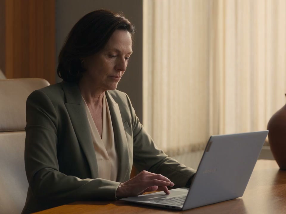 A clinic owner considering her work at a laptop in a sunlit office